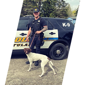 Tulalip Police Department Officer Jordan with K9 Buster posing in front of a patrol car. 