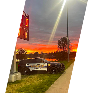 A Tulalip patrol car is parked on the grass with a brilliant sunset on the horizon displaying bright colors of yellow and orange